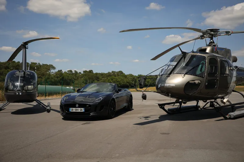 Jaguar F-Type V6 cabriolet noire entre deux hélicoptères sur un tarmac